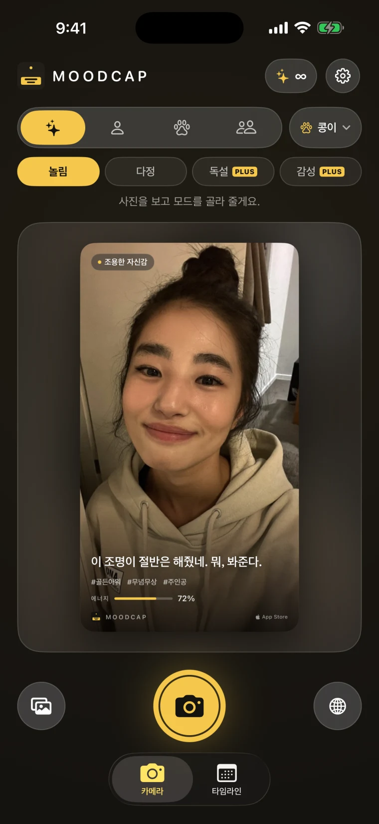 무드캡 홈 화면. 모드 선택 옆에 &lsquo;콩이&rsquo; 프로필 칩이 있고, 그 아래 말투 줄에 놀림·다정·독설·감성이 있으며 뒤의 두 개에는 PLUS 표시가 붙어 있다. 아래에는 후드티를 입고 웃는 여성의 카드 &lsquo;이 조명이 절반은 해줬네. 뭐, 봐준다.&rsquo;와 셔터 버튼, 카메라·타임라인 탭이 보인다.